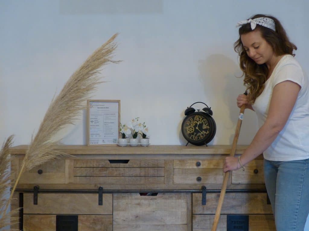 Ménage balaye une pièce, devant un bahut en bois